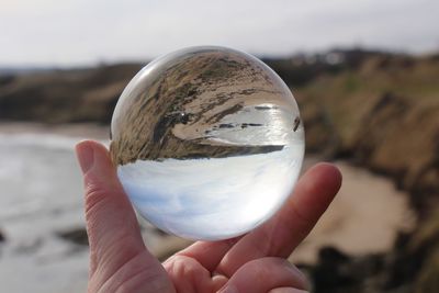 Close-up of hand holding crystal ball against sky