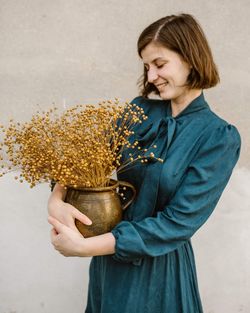 Woman holding flower standing against wall