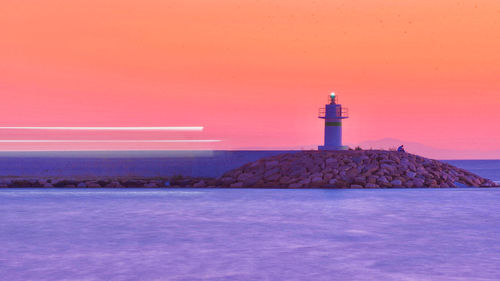 Lighthouse by sea against sky during sunset