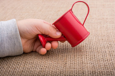 Close-up of child holding toy watering can on burlap