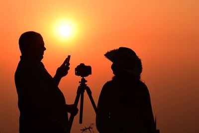 Silhouette people photographing orange sky during sunset