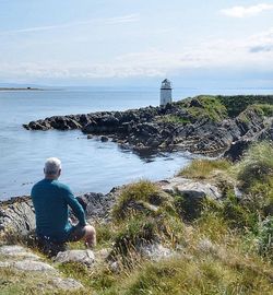 Rear view of man looking at sea shore against sky