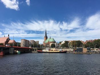 View of buildings by river against cloudy sky