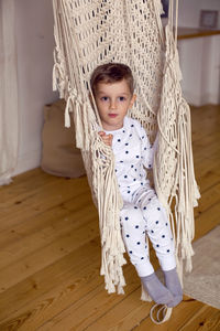 Little boy in the gray pajamas in knitted ropes of the hammock house
