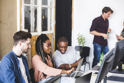 Female it expert showing laptop to professional male hackers at workplace