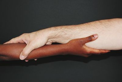 Close-up of man and woman holding hands against black background