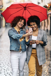 Young couple holding hands while standing on umbrella during rain