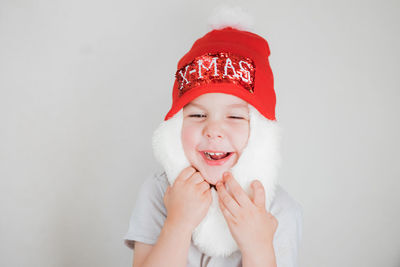 Toddler boy in santa claus costume with beard and red hat on white background