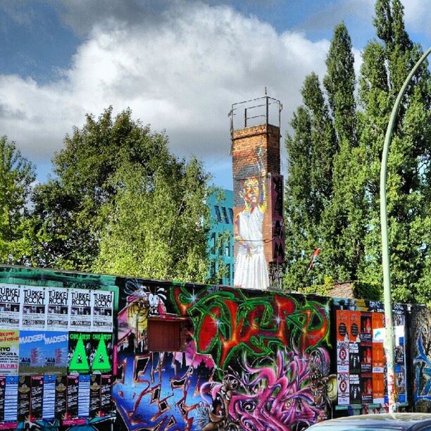 tree, built structure, architecture, sky, building exterior, graffiti, multi colored, cloud - sky, day, railing, outdoors, cloud, no people, art, wall - building feature, text, growth, house, fence, art and craft