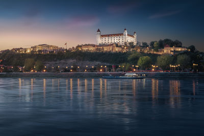 Buildings by river against sky at night