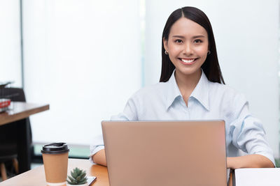 Portrait of smiling young businesswoman using laptop at office