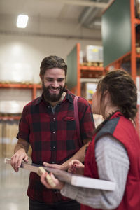 Happy male customer buying metal plank from saleswoman in hardware store