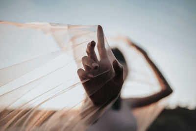 Low angle view of woman holding scarf against sky at sunset