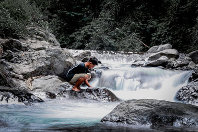 Man looking away while standing on rock by river