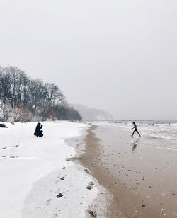 Photographer photographing at snow covered beach against sky