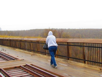 Rear view of man standing on railing against clear sky