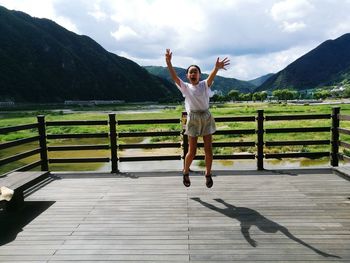 Full length of cheerful with arms raised jumping against sky