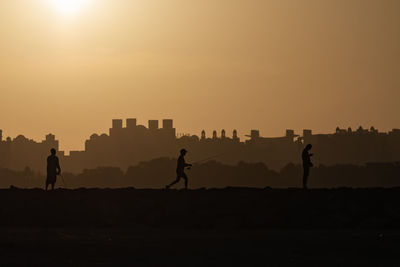 Silhouette people on field against sky during sunset