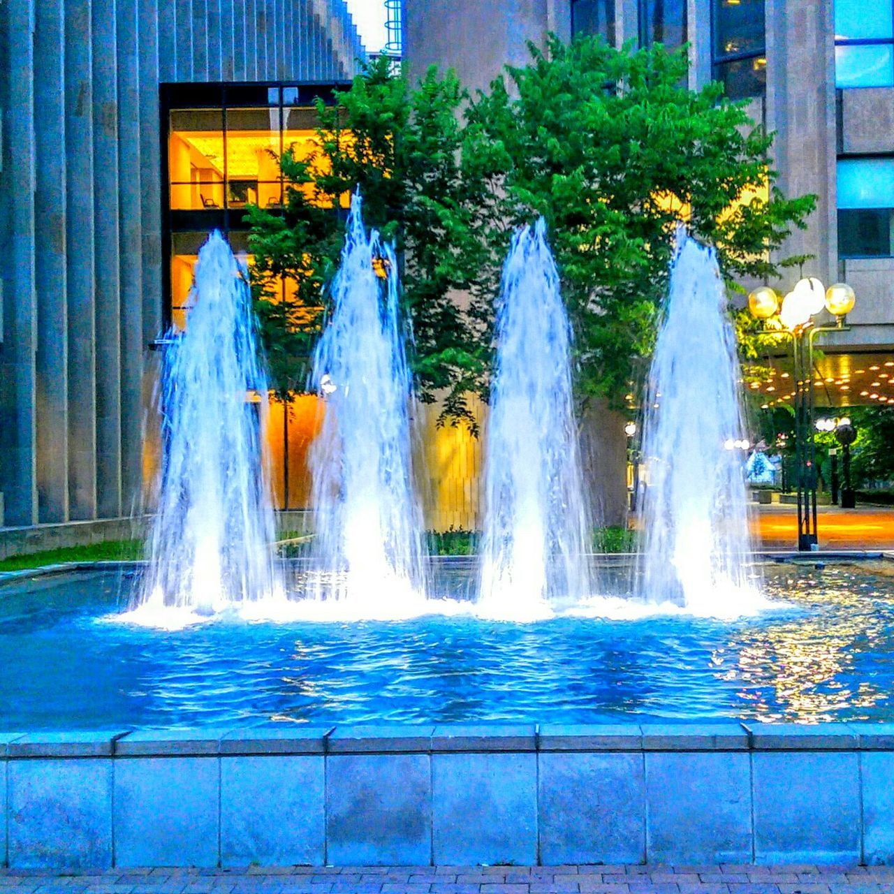 fountain, water, motion, long exposure, spraying, splashing, built structure, architecture, waterfall, flowing water, building exterior, blurred motion, flowing, reflection, waterfront, tree, outdoors, park - man made space, multi colored, pond