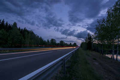 Empty road by trees against sky