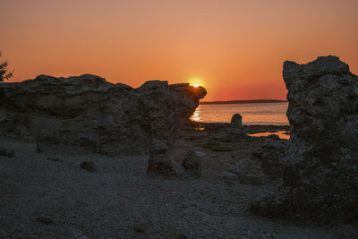Rock formation on beach against sky during sunset