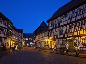 Illuminated street amidst buildings against clear sky at night