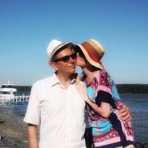 Woman kissing man on cheek while standing against clear blue sky