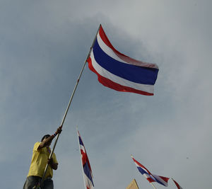 Low angle view of man with thai flag protesting against sky