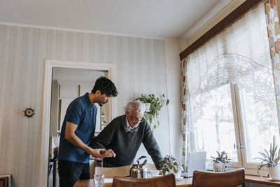 Male caregiver helping senior man walking at home