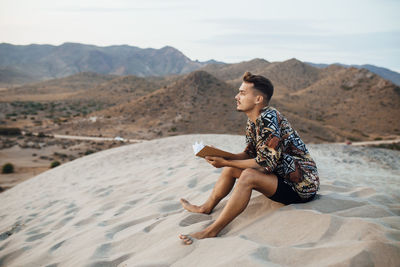 Young man contemplating while holding book in desert at almeria, tabernas, spain