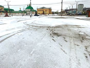 Snow covered road by buildings in city