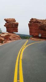 Empty road by rock formations against clear sky