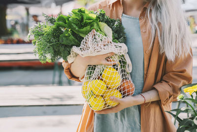 Customer holding leafy vegetables and lemons in mesh bag at local market