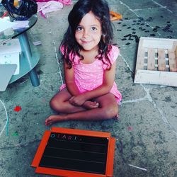 Portrait of smiling girl with slate sitting on floor at home