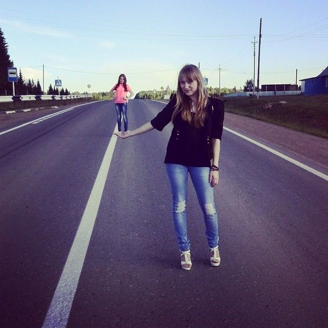 lifestyles, casual clothing, transportation, street, road, full length, leisure activity, front view, standing, person, young adult, the way forward, looking at camera, portrait, walking, sky, road marking, young women