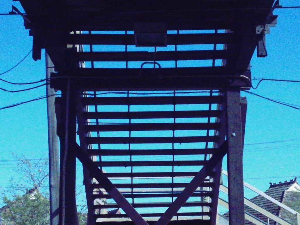 built structure, architecture, railing, blue, connection, low angle view, transportation, building exterior, bridge - man made structure, staircase, day, cable, steps, sunlight, outdoors, metal, railroad station, building, reflection, power line