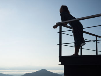 Low angle view of woman standing by railing against sky