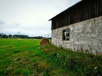 Abandoned house on grassy field against cloudy sky