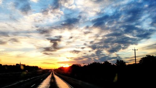 Road passing through landscape against cloudy sky at sunset