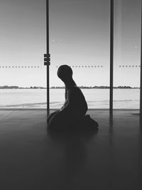 Silhouette woman sitting by window against sky