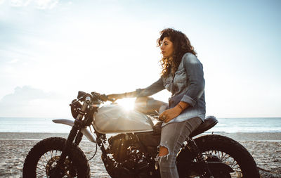 Woman sitting on motor cycle on beach against sky