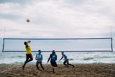 People playing soccer on beach against sky
