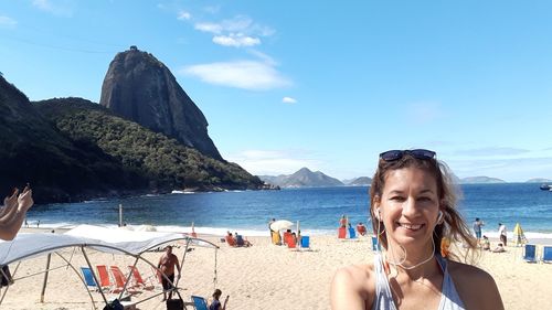 Portrait of smiling woman listening music at beach against sky during summer