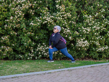 Full length of senior woman doing lunges against flowing plants in park