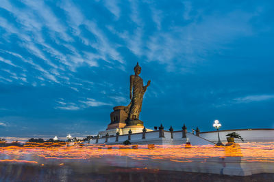 Light trails and statue against blue sky