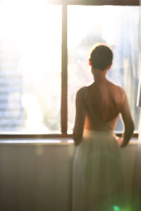 Rear view of shirtless man looking through window