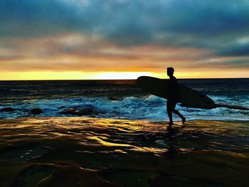 Silhouette man standing on beach against sky during sunset