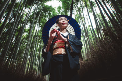 Mature woman with umbrella standing amidst trees