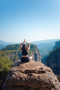 Rear view of woman sitting on rock against sky