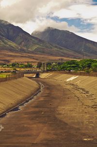 Sewer by mountains against cloudy sky